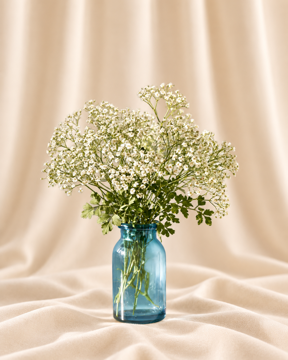 White gypsophila (baby's breath) + leafy greenery in a blue glass jar.