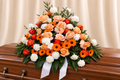 Peach, orange and red roses + orange gerberas + white carnations in a casket spray; no baby's breath.
